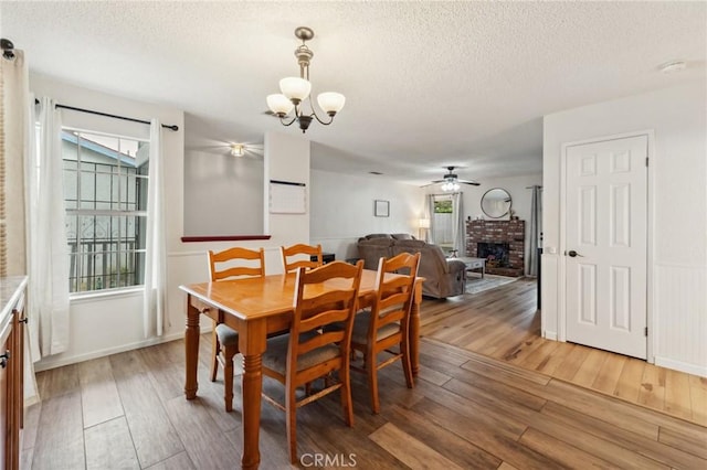 1045 Clover Ln, Hanford, CA 93230 - dining area with a chandelier, light wood-type flooring, a ceiling fan, a brick fireplace, and a textured ceiling