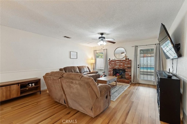 1045 Clover Ln, Hanford, CA 93230 - living room with a textured ceiling, light wood finished floors, ceiling fan, a brick fireplace, and healthy amount of natural light