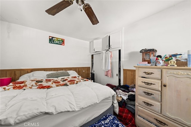 bedroom featuring wainscoting, wooden walls, and ceiling fan