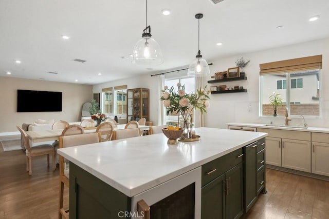 kitchen featuring visible vents, wood finished floors, a kitchen island, a sink, and decorative light fixtures