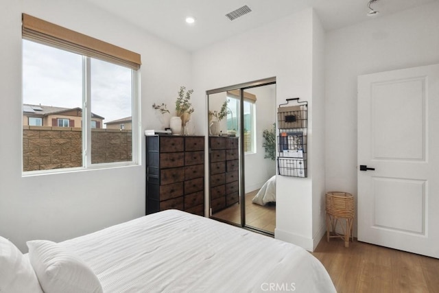bedroom with a closet, recessed lighting, wood finished floors, and visible vents