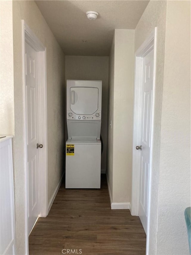 clothes washing area with baseboards, laundry area, wood finished floors, and stacked washer and clothes dryer