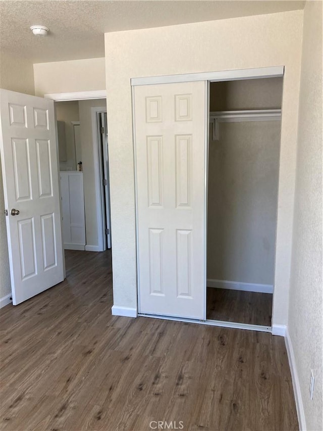 unfurnished bedroom with a textured ceiling, baseboards, a closet, and wood finished floors