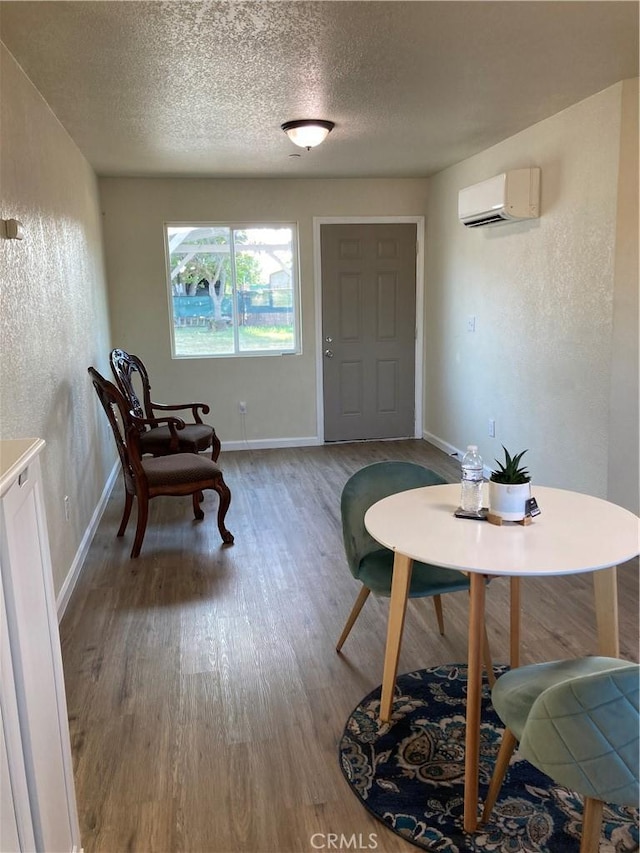 interior space with wood finished floors, a textured ceiling, baseboards, and a wall mounted AC