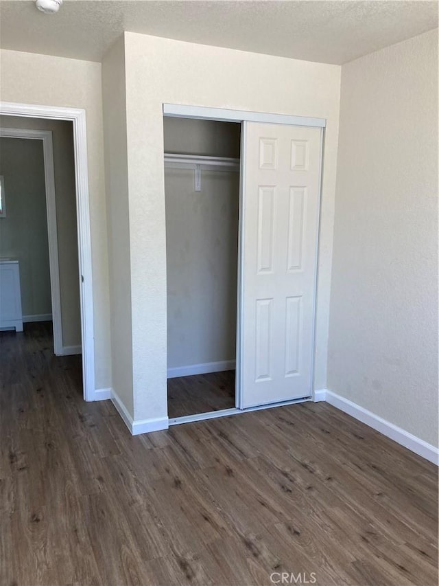 unfurnished bedroom featuring baseboards, a closet, and dark wood-style floors
