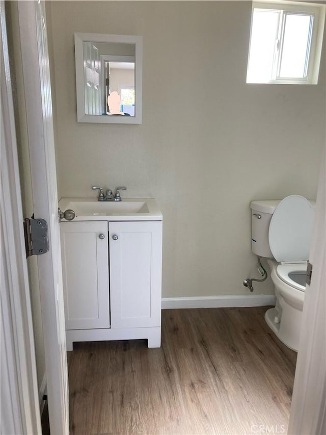 half bathroom with toilet, baseboards, wood finished floors, and vanity