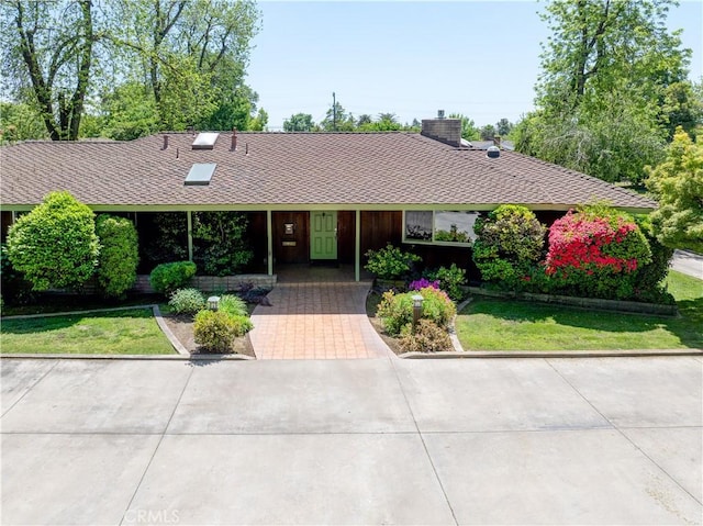 ranch-style house with a chimney, a shingled roof, and a front yard