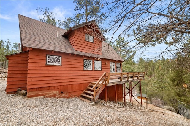 back of property with a deck, stairs, and a shingled roof