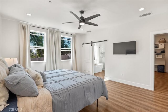 bedroom featuring a walk in closet, wood finished floors, a barn door, and baseboards