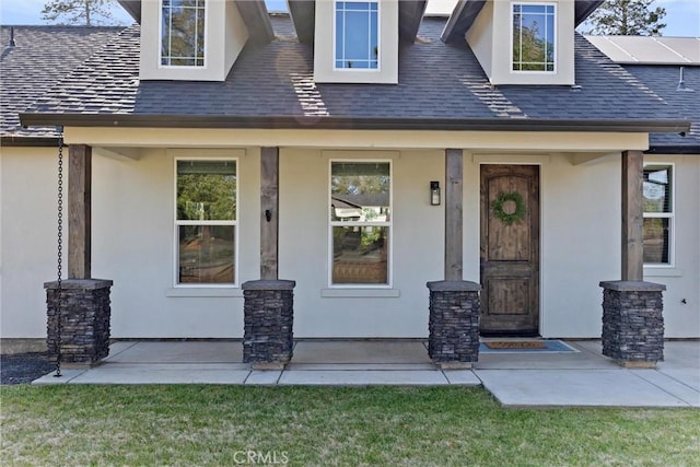 view of exterior entry featuring a porch, a shingled roof, and stucco siding