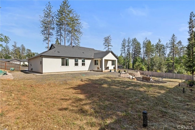 back of property featuring an outdoor fire pit, a fenced backyard, stucco siding, and a yard