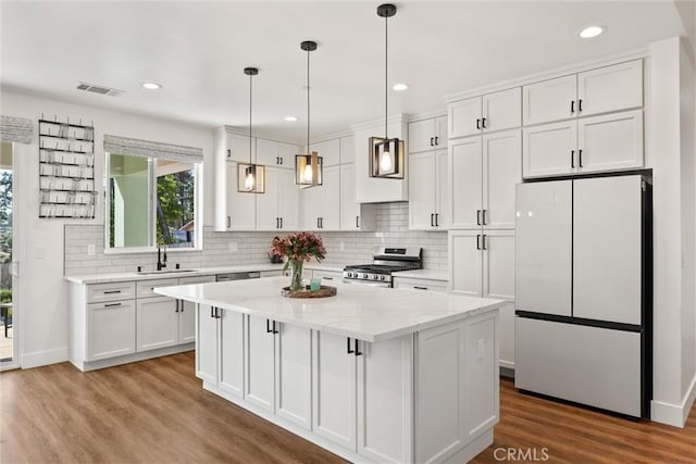 kitchen with stainless steel gas range, visible vents, white cabinets, and freestanding refrigerator