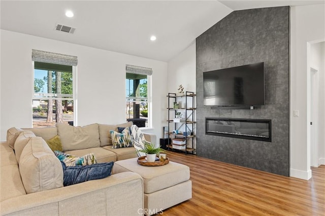 living area with a wealth of natural light, wood finished floors, a tile fireplace, and lofted ceiling