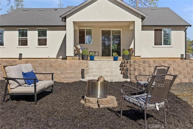 back of property with an outdoor fire pit, stucco siding, and roof with shingles