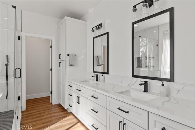 bathroom featuring a marble finish shower, a sink, double vanity, and wood finished floors