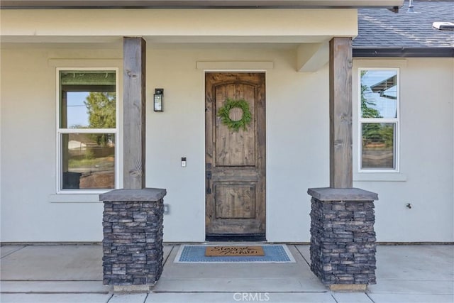 view of exterior entry with covered porch, stucco siding, and roof with shingles