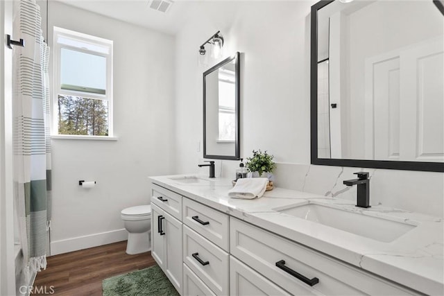 bathroom featuring wood finished floors, toilet, a sink, baseboards, and visible vents