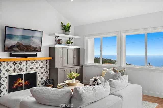 living area with baseboards, light wood-type flooring, a tile fireplace, and lofted ceiling