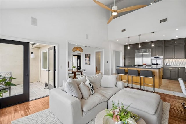 living room featuring visible vents, high vaulted ceiling, light wood finished floors, and a ceiling fan