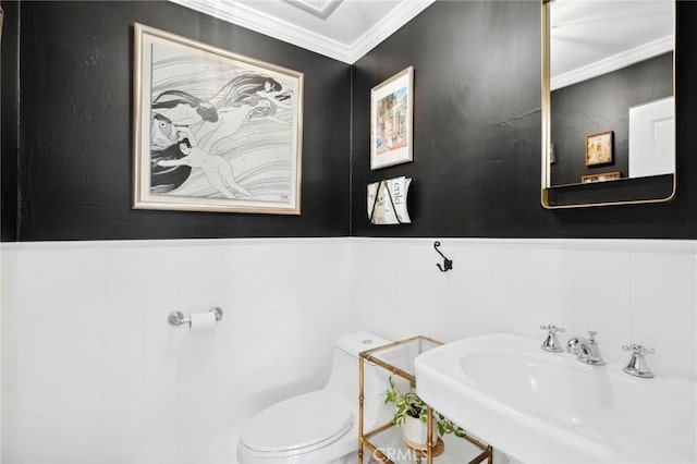 bathroom featuring ornamental molding, a wainscoted wall, a sink, and toilet