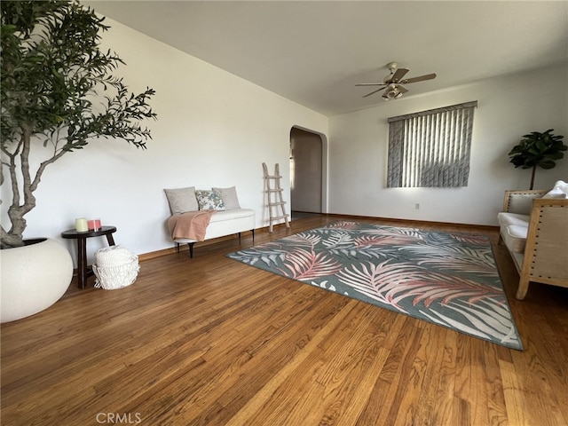 sitting room featuring arched walkways, baseboards, a ceiling fan, and wood finished floors