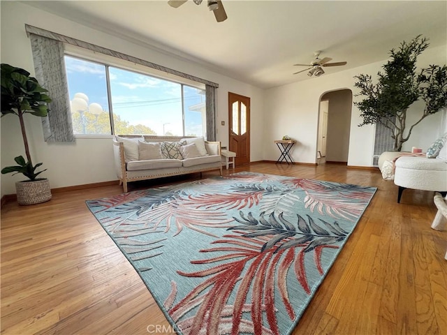 living room featuring baseboards, arched walkways, ceiling fan, and wood finished floors