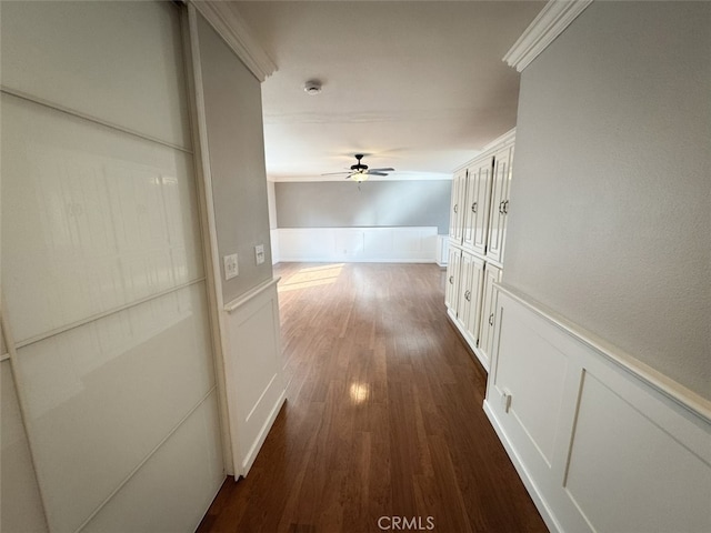 corridor with dark wood-type flooring, a decorative wall, crown molding, and wainscoting