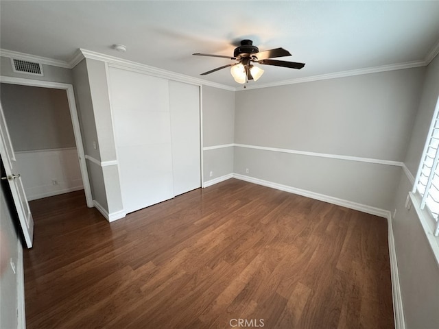 unfurnished bedroom featuring a closet, visible vents, baseboards, ornamental molding, and dark wood finished floors