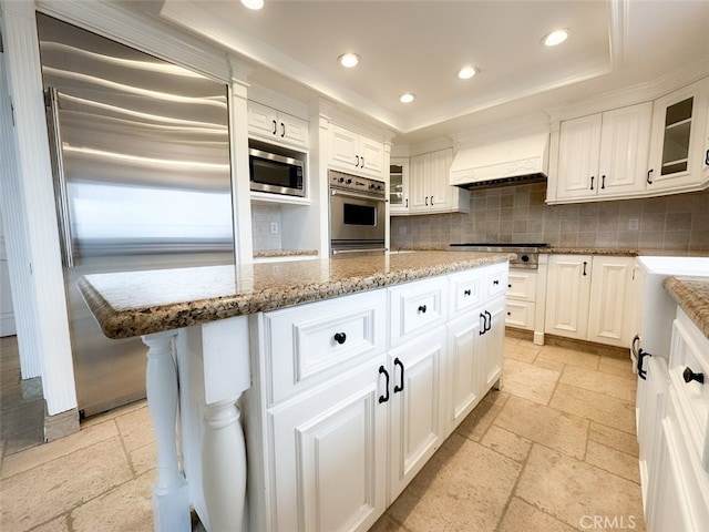 kitchen with recessed lighting, decorative backsplash, built in appliances, stone tile floors, and premium range hood