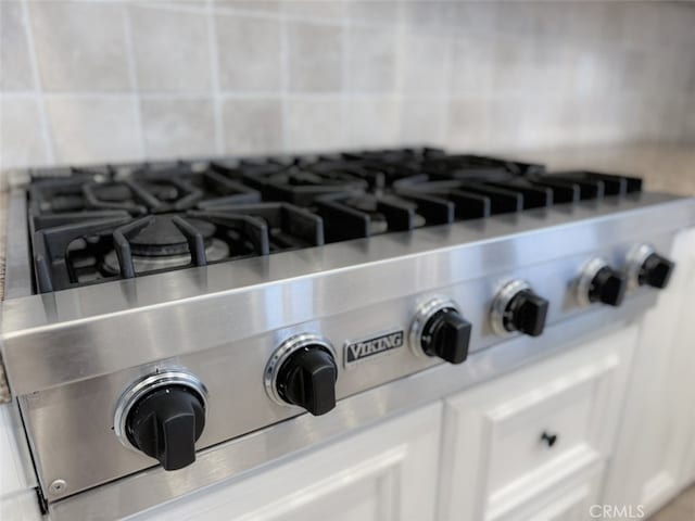 room details with decorative backsplash, white cabinets, stainless steel gas stovetop, light countertops, and luxury stove
