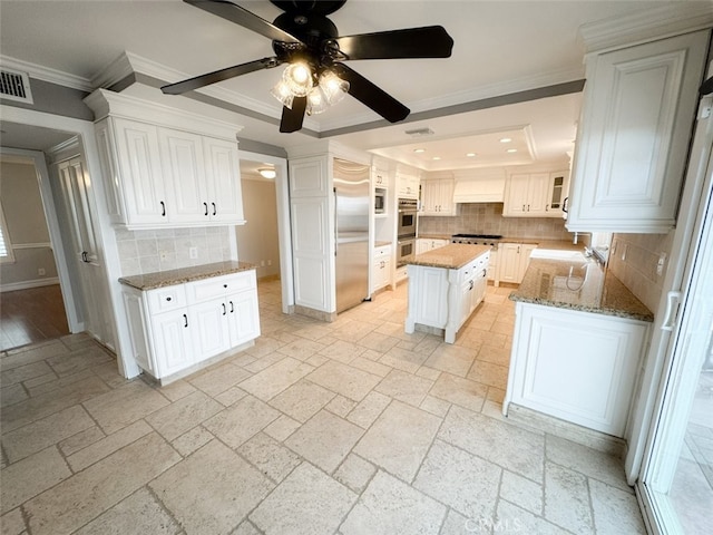 kitchen with decorative backsplash, custom range hood, built in appliances, a raised ceiling, and a ceiling fan