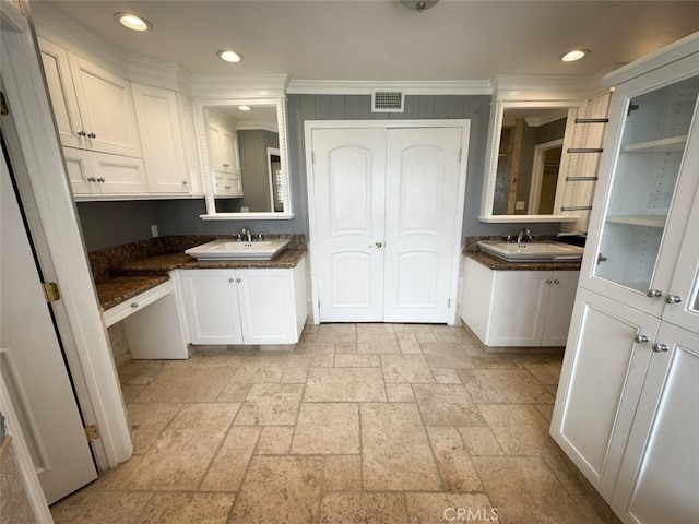 kitchen featuring dark countertops, a sink, stone tile floors, visible vents, and crown molding