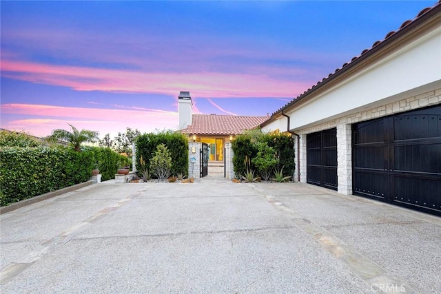 single story home featuring concrete driveway, a chimney, a tiled roof, stucco siding, and a garage