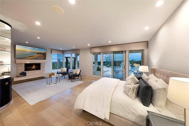 bedroom with light wood-style floors, a warm lit fireplace, access to outside, and recessed lighting