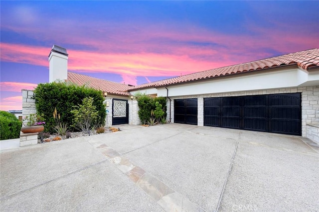 mediterranean / spanish house with a tile roof, a garage, a gate, concrete driveway, and stucco siding
