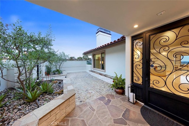 doorway to property with a chimney, stucco siding, a tiled roof, and a patio area