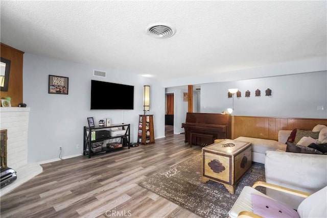 living room with a brick fireplace, a textured ceiling, visible vents, and wood finished floors