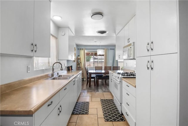 kitchen featuring white cabinetry, a sink, light countertops, white appliances, and light tile patterned flooring