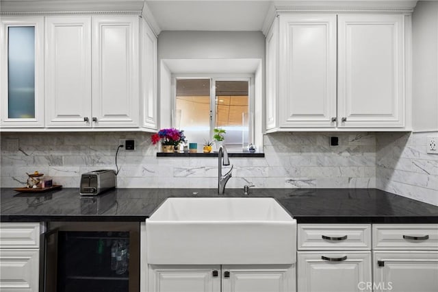 kitchen featuring wine cooler, a sink, white cabinets, and dark countertops
