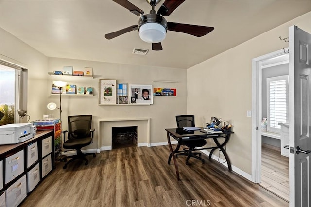 office with baseboards, visible vents, wood finished floors, and a ceiling fan