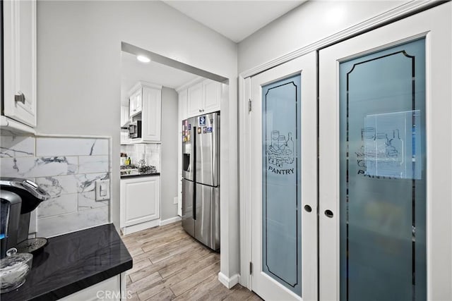 kitchen featuring stainless steel appliances, light wood-type flooring, white cabinetry, baseboards, and dark countertops