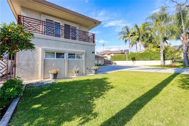 rear view of property with fence, a yard, stucco siding, and a balcony