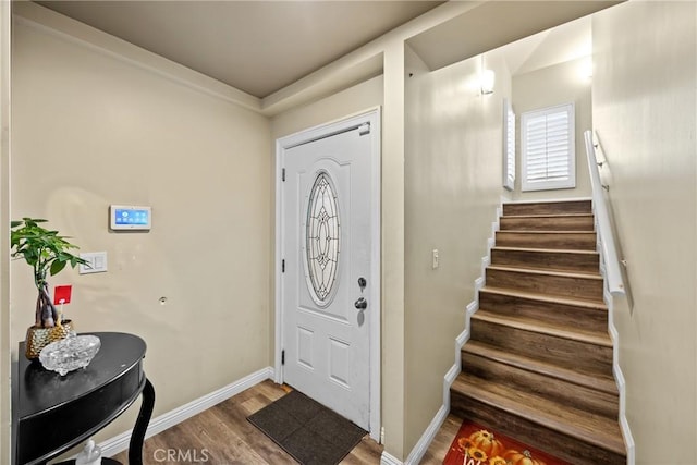 entryway featuring baseboards, wood finished floors, and stairs