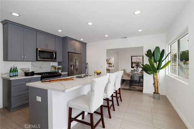 kitchen featuring appliances with stainless steel finishes, light stone countertops, a sink, gray cabinetry, and a breakfast bar
