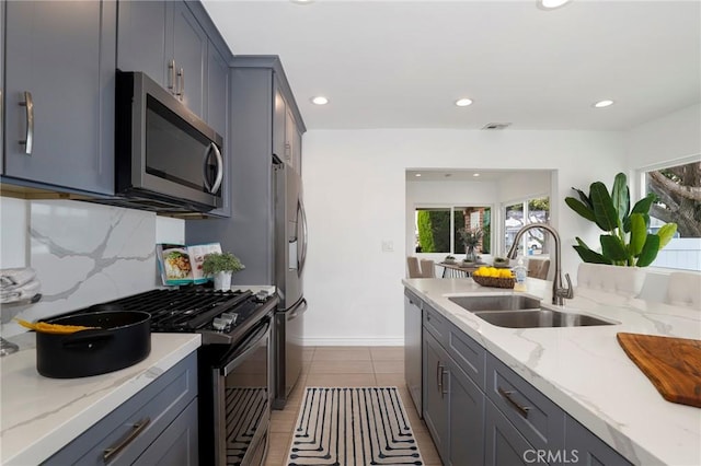 kitchen featuring light stone counters, a sink, stainless steel appliances, recessed lighting, and backsplash