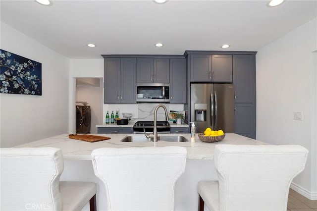 kitchen with washer and dryer, light stone countertops, appliances with stainless steel finishes, a sink, and recessed lighting