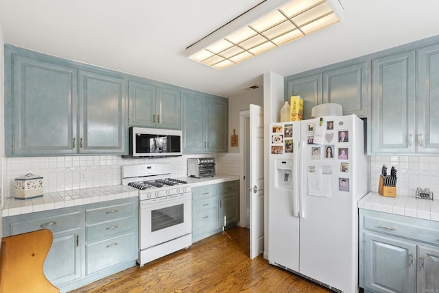8140 Pasadena Ave, La Mesa, CA 91941 - kitchen with wood finished floors, white appliances, tile counters, visible vents, and backsplash