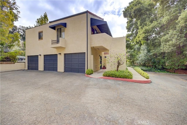 exterior space featuring a garage, stucco siding, driveway, and a balcony