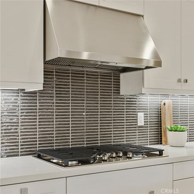 interior details with white cabinets, stainless steel gas stovetop, wall chimney range hood, and decorative backsplash