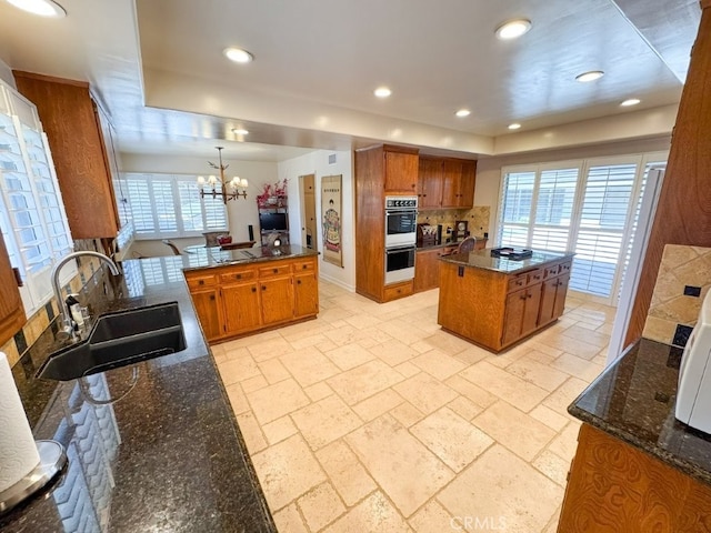 kitchen featuring backsplash, a sink, brown cabinets, and a chandelier